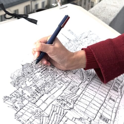 Gros plan d'une main avec stylo dessinant les toits de Paris