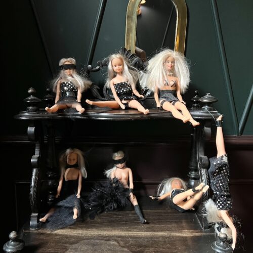 Des poupées Barbie habillées de tenues libertines, sur une étagère.