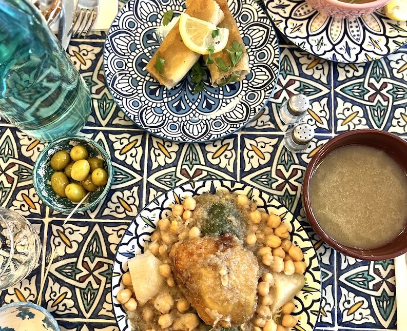 Différents plats algériens servis sur une table de carreaux traditionnels.