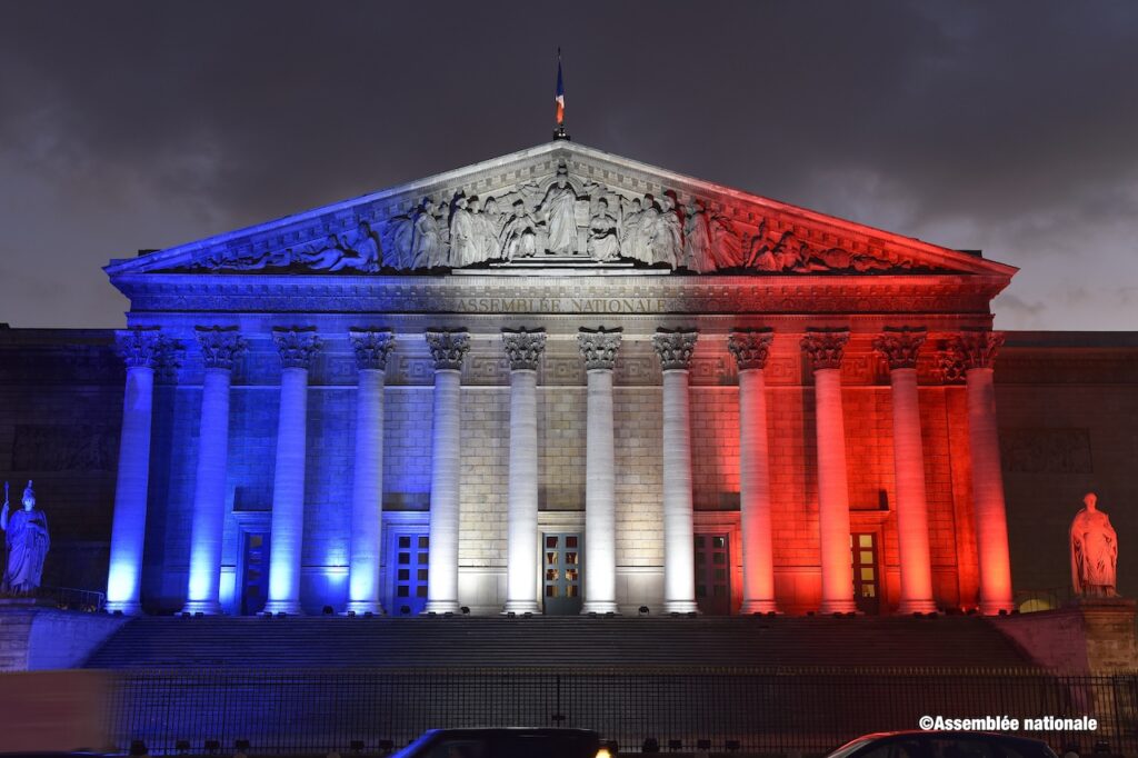 Photo des colonnades de l'Assemblée nationale éclairée de bleu blanc rouge