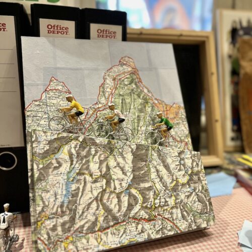 Une carte de montagne en 2D fabriquée à partir de bouts de cartes Michelin avec des figurines de vélos à l'assaut de la côte