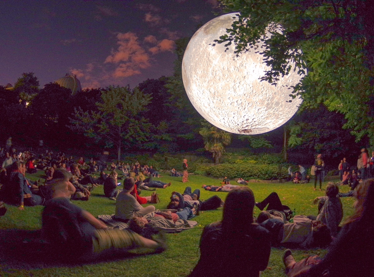 Installation "Museum of the Moon" de l'artiste Luke Jerram : une structure représentant une lune en suspension est regardée par des spectateurs allongés dans un jardin.