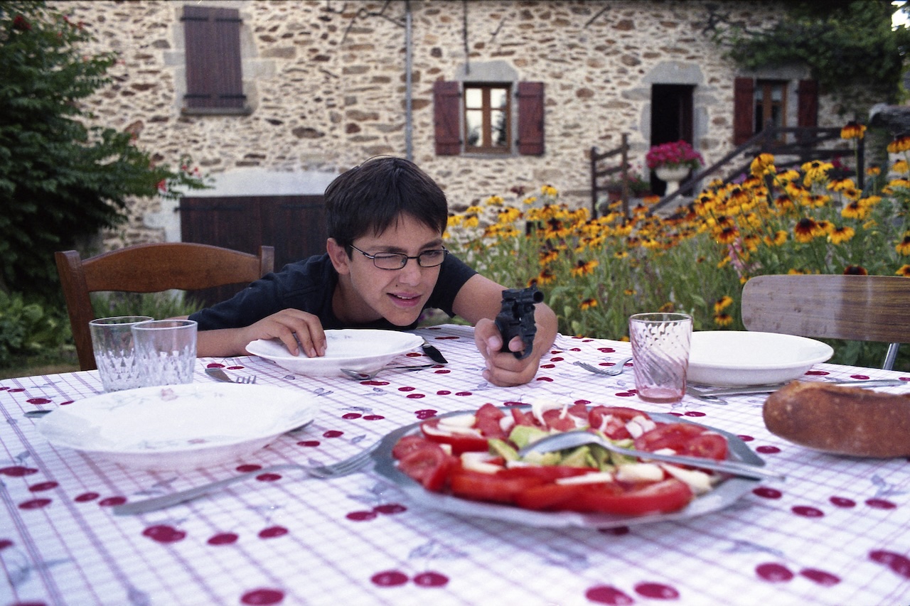 Photo de Laura Lafon Cadilhac présentant son cousin qui joue avec une arme en jouet avant de manger dans le jardin.