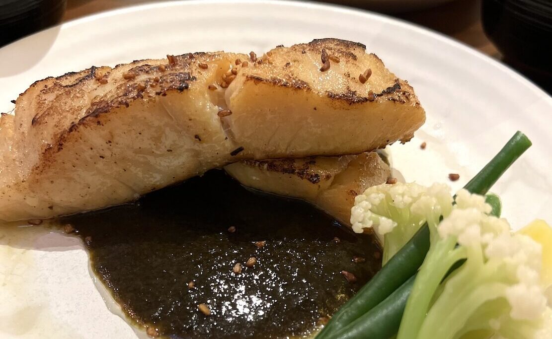 Assiette avec un lieu jaune, sauce nori et petits légumes