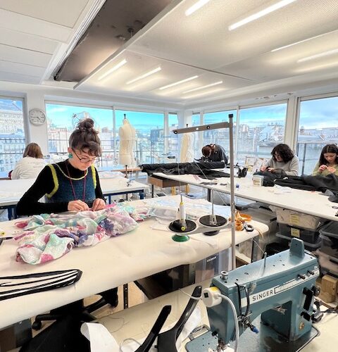 Vue générale sur l'atelier avec table de découpe, couturière et au premier plan une machine singer