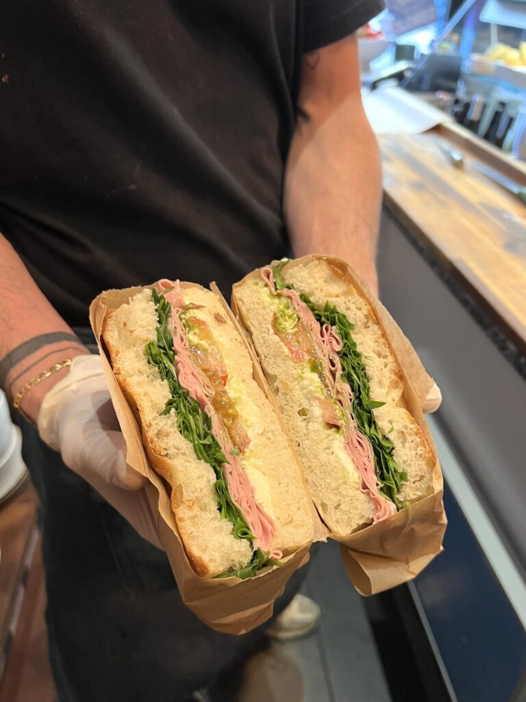 Focaccia coupée en deux avec sa garniture : Mortadella, crème de burrata, tomates séchées, roquette