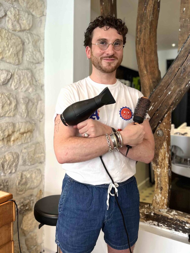 Benjamin, coiffeur avec une brosse et un sèche cheveu en mains.