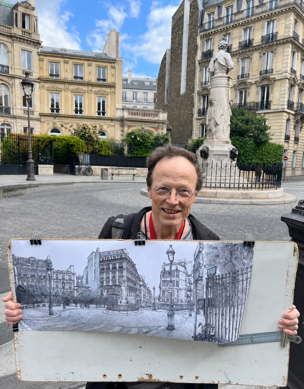 Christian Baillard pose devant la Place Saint Georges avec son dessin à l'encre la reproduisant